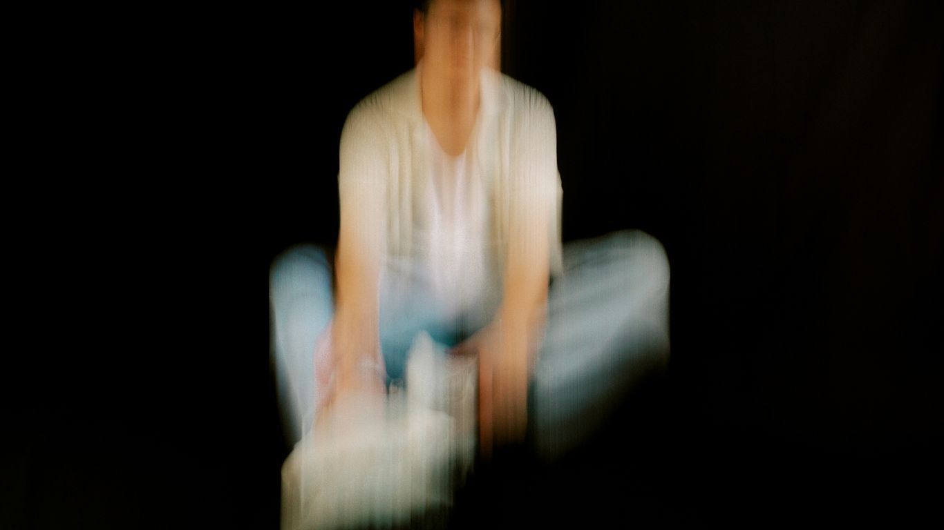 A blurred person is sitting in a dark space.