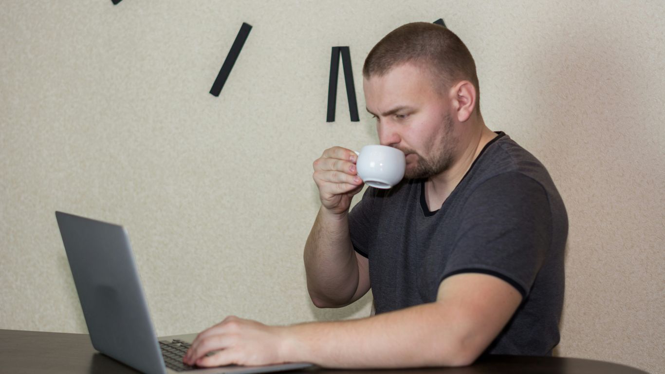 a man drinking a cup of coffee while using a laptop