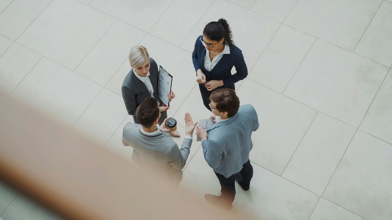 Four business people talking in a modern office lobby.