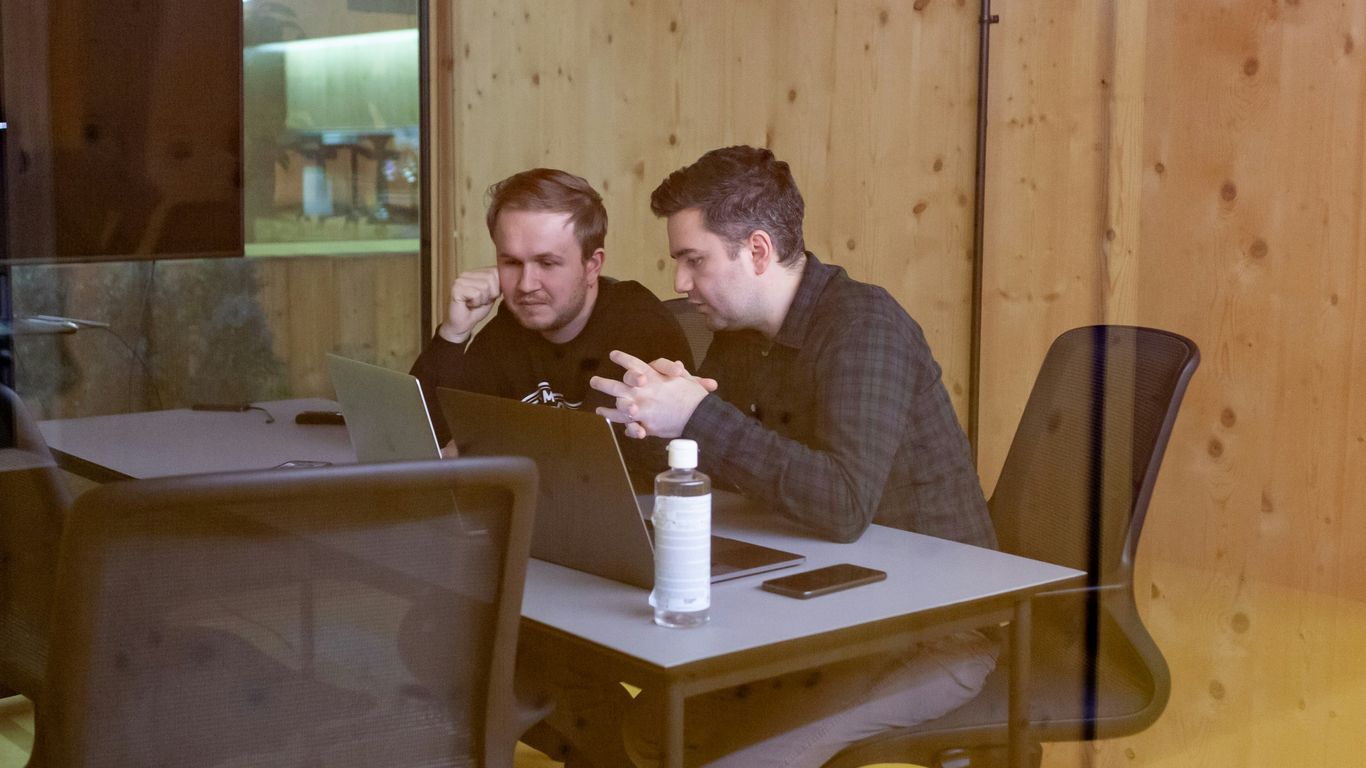 two men sitting at a table with a laptop