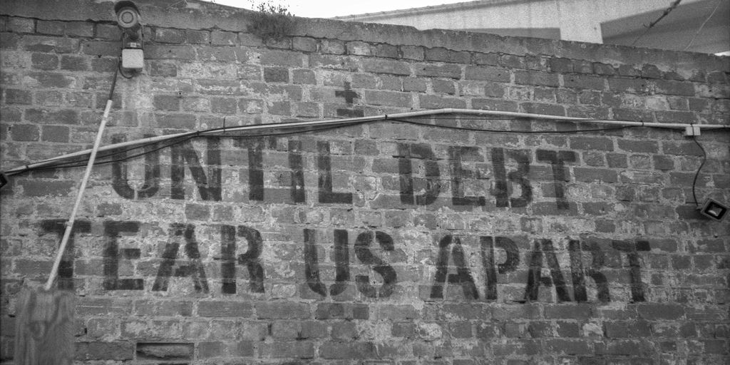 a sign on a brick wall that says until debt tears apart