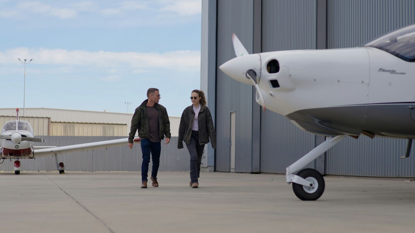 Two people walking on tarmac near small airplanes