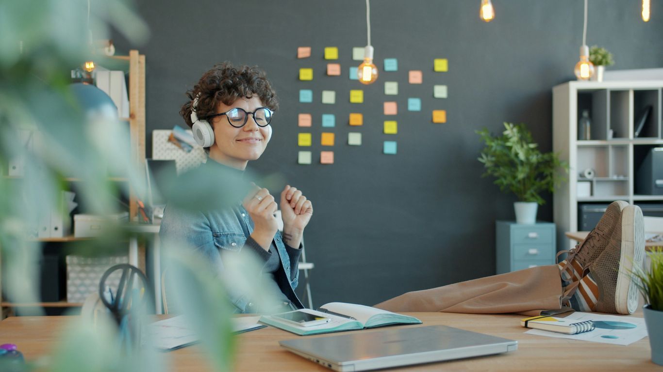 Young woman with headphones happily working at desk.