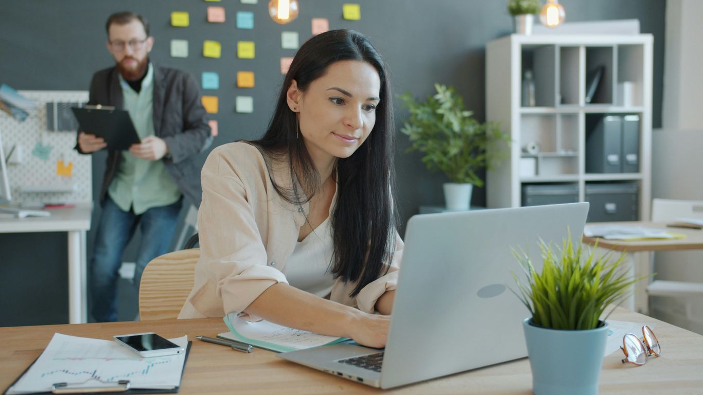 Woman working on laptop with man behind her