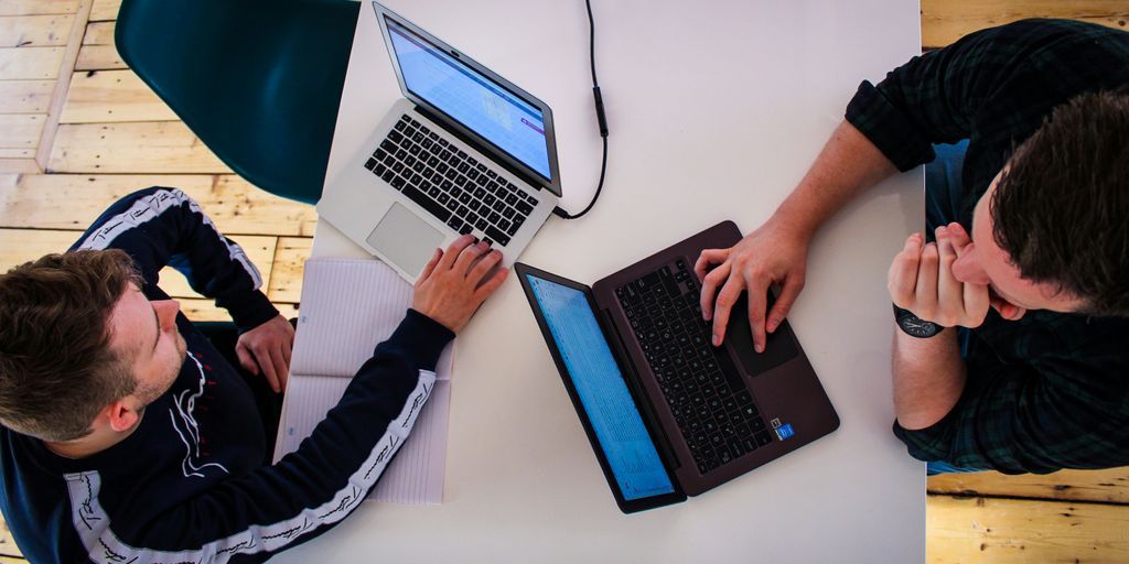 two men sitting at a table working on laptops
