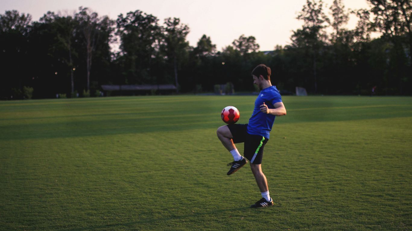 man juggling ball on grass field