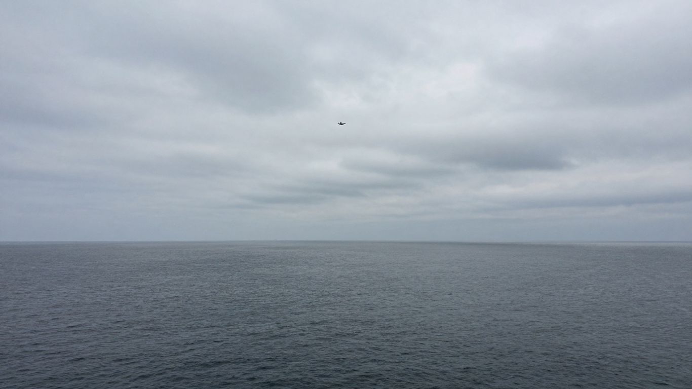 Ocean expanse with a distant airplane, evoking mystery.