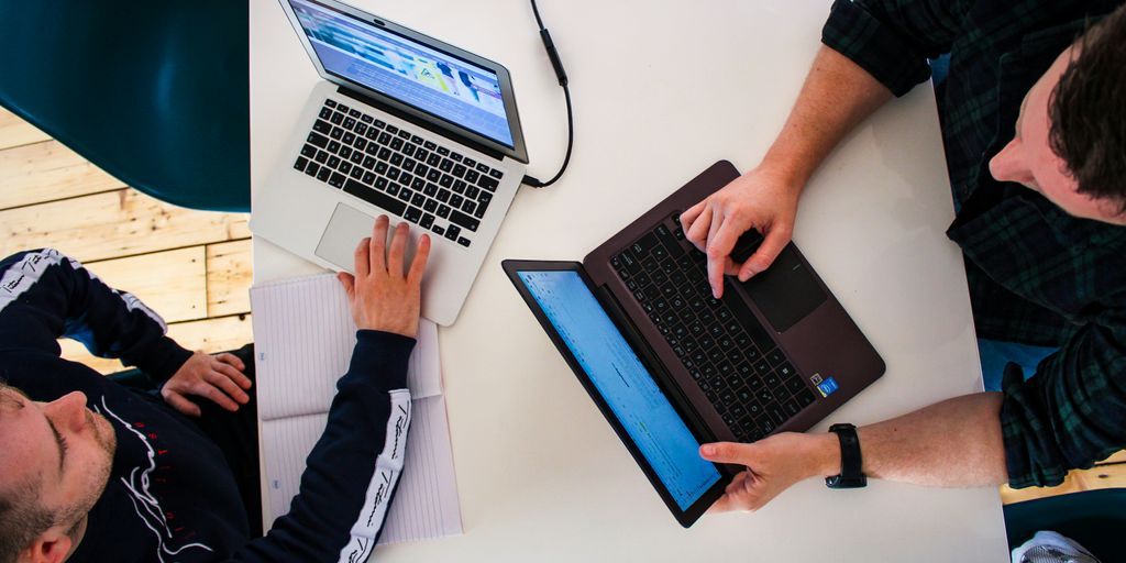 two men sitting at a table working on laptops